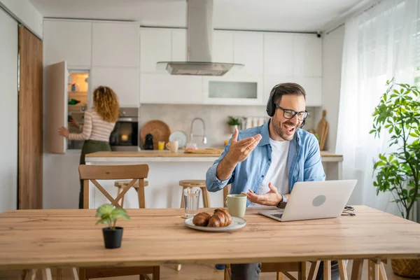 stock image One man caucasian male freelancer work from home with headphones on his head on laptop computer customer support happy smile confident his wife stand in the background