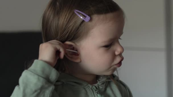 白人の女の子2歳の幼児は綿棒の芽を使用して耳をきれいにしますスローモーション — ストック動画