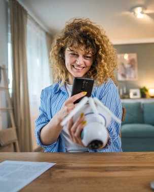 Yetişkin bir beyaz kadın güvenlik kameralarını ayarlar, talimatları okur ve etkinleştirme kodunu kopyalamak için akıllı telefonu kullanır.