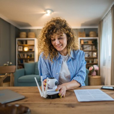 Yetişkin bir beyaz kadın güvenlik kameralarını ayarlar, talimatları okur ve etkinleştirme kodunu kopyalamak için akıllı telefonu kullanır.