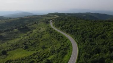 Sırbistan 'da yeşillik ve manzara taşımacılığı ve seyahat konseptiyle çevrili dolambaçlı yol boyunca giden yaz aracı otomobili sırasında bir dağ sırasındaki eğimli asfalt bir yolun hava aracı görüntüleri
