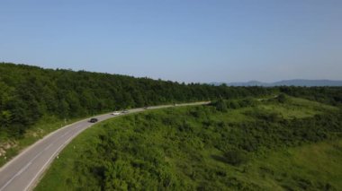 Sırbistan 'da yeşillik ve manzara taşımacılığı ve seyahat konseptiyle çevrili dolambaçlı yol boyunca giden yaz aracı otomobili sırasında bir dağ sırasındaki eğimli asfalt bir yolun hava aracı görüntüleri