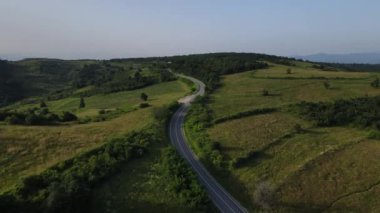 Sırbistan 'da yeşillik ve manzara taşımacılığı ve seyahat konseptiyle çevrili dolambaçlı yol boyunca giden yaz aracı otomobili sırasında bir dağ sırasındaki eğimli asfalt bir yolun hava aracı görüntüleri