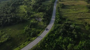 Sırbistan 'da yeşillik ve manzara taşımacılığı ve seyahat konseptiyle çevrili dolambaçlı yol boyunca giden yaz aracı otomobili sırasında bir dağ sırasındaki eğimli asfalt bir yolun hava aracı görüntüleri