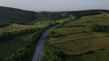 Sırbistan 'da yeşillik ve manzara taşımacılığı ve seyahat konseptiyle çevrili dolambaçlı yol boyunca giden yaz aracı otomobili sırasında bir dağ sırasındaki eğimli asfalt bir yolun hava aracı görüntüleri