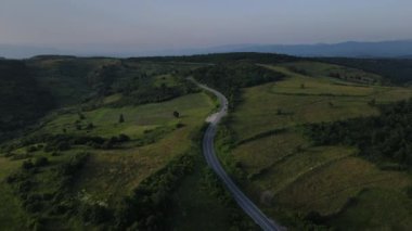 Sırbistan 'da yeşillik ve manzara taşımacılığı ve seyahat konseptiyle çevrili dolambaçlı yol boyunca giden yaz aracı otomobili sırasında bir dağ sırasındaki eğimli asfalt bir yolun hava aracı görüntüleri