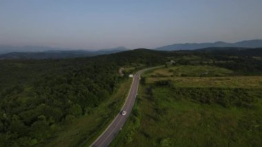 Sırbistan 'da yeşillik ve manzara taşımacılığı ve seyahat konseptiyle çevrili dolambaçlı yol boyunca giden yaz aracı otomobili sırasında bir dağ sırasındaki eğimli asfalt bir yolun hava aracı görüntüleri