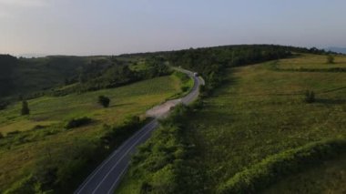 Sırbistan 'da yeşillik ve manzara taşımacılığı ve seyahat konseptiyle çevrili dolambaçlı yol boyunca giden yaz aracı otomobili sırasında bir dağ sırasındaki eğimli asfalt bir yolun hava aracı görüntüleri