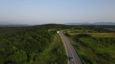 Sırbistan 'da yeşillik ve manzara taşımacılığı ve seyahat konseptiyle çevrili dolambaçlı yol boyunca giden yaz aracı otomobili sırasında bir dağ sırasındaki eğimli asfalt bir yolun hava aracı görüntüleri