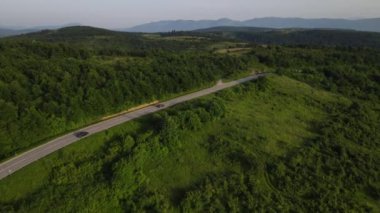 Sırbistan 'da yeşillik ve manzara taşımacılığı ve seyahat konseptiyle çevrili dolambaçlı yol boyunca giden yaz aracı otomobili sırasında bir dağ sırasındaki eğimli asfalt bir yolun hava aracı görüntüleri
