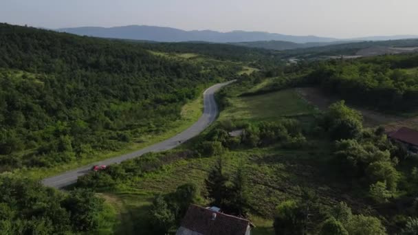 緑と風景輸送と旅行のコンセプトに囲まれたセルビアの曲がりくねった道に沿って運転夏の車の中で山の範囲に湾曲したアスファルト道路の空中ドローン映像 — ストック動画