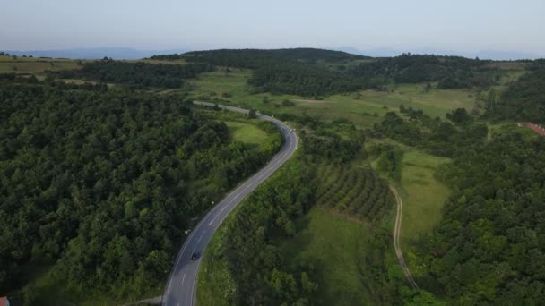 緑と風景輸送と旅行のコンセプトに囲まれたセルビアの曲がりくねった道に沿って運転夏の車の中で山の範囲に湾曲したアスファルト道路の空中ドローン映像 — ストック動画