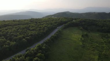 Sırbistan 'da yeşil ve manzara taşımacılığı ve seyahat konseptiyle çevrili dolambaçlı yol boyunca giden bahar aracı kamyonları sırasında bir dağ sırasındaki eğri asfalt bir yolun hava aracı görüntüleri