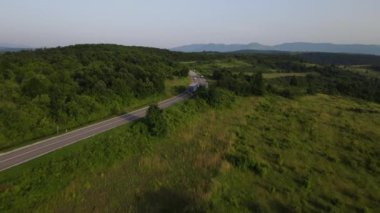 Sırbistan 'da yeşil ve manzara taşımacılığı ve seyahat konseptiyle çevrili dolambaçlı yol boyunca giden bahar aracı kamyonları sırasında bir dağ sırasındaki eğri asfalt bir yolun hava aracı görüntüleri