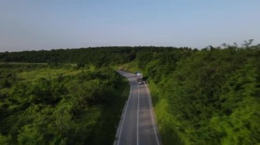 Sırbistan 'da yeşil ve manzara taşımacılığı ve seyahat konseptiyle çevrili dolambaçlı yol boyunca giden bahar aracı kamyonları sırasında bir dağ sırasındaki eğri asfalt bir yolun hava aracı görüntüleri
