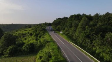 Sırbistan 'da yeşil ve manzara taşımacılığı ve seyahat konseptiyle çevrili dolambaçlı yol boyunca giden bahar aracı kamyonları sırasında bir dağ sırasındaki eğri asfalt bir yolun hava aracı görüntüleri