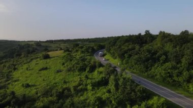 Sırbistan 'da yeşil ve manzara taşımacılığı ve seyahat konseptiyle çevrili dolambaçlı yol boyunca giden bahar aracı kamyonları sırasında bir dağ sırasındaki eğri asfalt bir yolun hava aracı görüntüleri