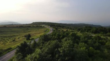 Sırbistan 'da yeşil ve manzara taşımacılığı ve seyahat konseptiyle çevrili dolambaçlı yol boyunca giden bahar aracı kamyonları sırasında bir dağ sırasındaki eğri asfalt bir yolun hava aracı görüntüleri