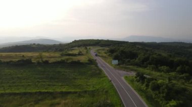 Sırbistan 'da yeşil ve manzara taşımacılığı ve seyahat konseptiyle çevrili dolambaçlı yol boyunca giden bahar aracı kamyonları sırasında bir dağ sırasındaki eğri asfalt bir yolun hava aracı görüntüleri