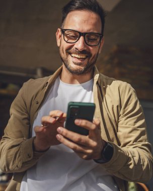 Beyaz tenli, sakallı ve gözlüklü bir adam güneşli bir günde açık havada oturur. Tişört giyer, cep telefonu kullanır. SMS mesajları atar, internete girer, internetten arama yapar.