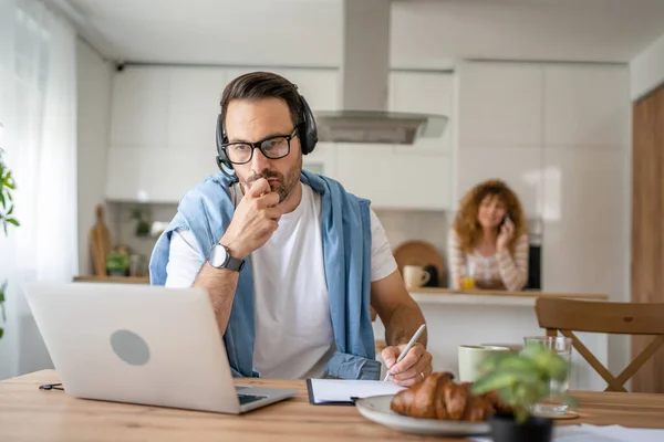 一名男子在家里工作 头上戴着耳机 头戴手提电脑 他的男性自由撰稿人支持认真考虑妻子的处境 — 图库照片