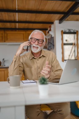 Gri sakallı, kıdemli beyaz bir erkek gündüzleri cep telefonuyla ev telefonundan konuşma fotokopisi çekiyor.