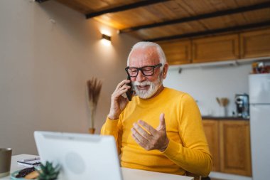 Gri sakallı, kıdemli beyaz bir erkek gündüzleri cep telefonuyla ev telefonundan konuşma fotokopisi çekiyor.