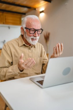 Beyaz üst düzey bir adam evde video görüşmesi yapmak için dizüstü bilgisayar kullanıyor.