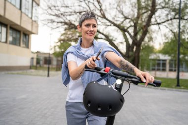Bir kadın olgun, yaşlı, beyaz, açık havada elektrikli scooterlı bir kadın. Gündüz kendine güvenen bir iş kadını modern alternatif ulaşım yöntemini kullanıyor. Gerçek insanlar uzayı kopyalıyor.