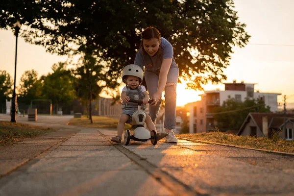 小さなCaucasian女の子幼児とともに母親遊び屋外で夏の夜に日没で3輪子供キックスクーター子供は保護ヘルメットを着用リアル人々コピースペースレジャー家族大人 — ストック写真