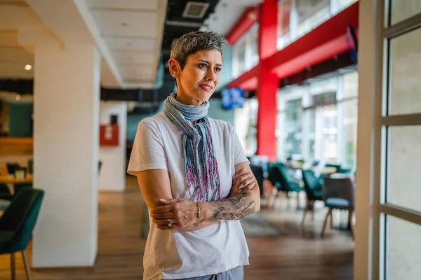 一位高年级 头戴短发的高加索女人独自站在咖啡店或餐馆里 手上戴着白衬衫纹身 自信而快乐地微笑着真实的人复制空间 — 图库照片
