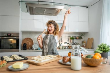 Genç, mutlu, beyaz bir kadın mutfak tebessümünde önlük takıyor. Karıştırıcı kaşıkla şarkı söylüyor.