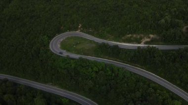 Sırbistan 'da yeşillik ve manzara taşımacılığı ve seyahat konseptiyle çevrili dolambaçlı yol boyunca giden yaz aracı otomobili sırasında bir dağ sırasındaki eğimli asfalt bir yolun hava aracı görüntüleri