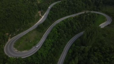 Sırbistan 'da yeşillik ve manzara taşımacılığı ve seyahat konseptiyle çevrili dolambaçlı yol boyunca giden yaz aracı otomobili sırasında bir dağ sırasındaki eğimli asfalt bir yolun hava aracı görüntüleri