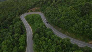 Sırbistan 'da yeşillik ve manzara taşımacılığı ve seyahat konseptiyle çevrili dolambaçlı yol boyunca giden yaz aracı otomobili sırasında bir dağ sırasındaki eğimli asfalt bir yolun hava aracı görüntüleri