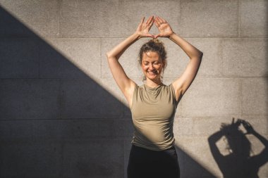 Yetişkin bir Kafkasyalı kadın yaz günü yoga pratiği yapıyor. Şehrin dışında, duvarın önünde. Gölge ve güneş gibi sağlıklı bir yaşam tarzı var.