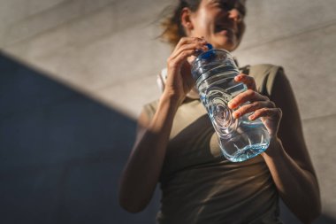 Bilinmeyen beyaz bir kadının göbeğine yaklaşın. Güneşli bir günde dışarıda beklerken plastik bir şişe su açın.