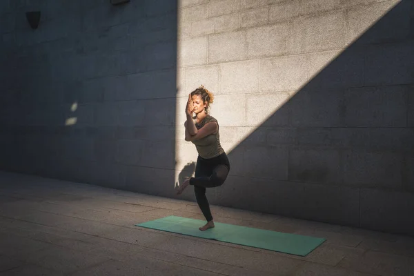 stock image One adult caucasian woman doing yoga practice in summer day outdoor in the city in front of the wall with shadow and sun healthy lifestyle wellbeing concept self care