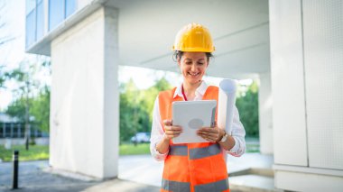 Mimar kadın inşaat mühendisi dışarıda duruyor ve modern bina duvarının önünde koruyucu başlık takıyor.