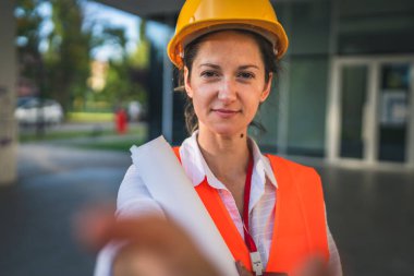 Mimar kadın inşaat mühendisi dışarıda duruyor. Modern bina duvarının önünde koruyucu kask takıyor ve batıda UGC kullanıcısı tarafından oluşturulan kendi portresi.