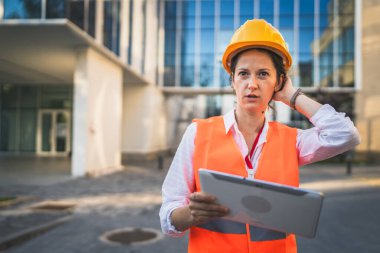 Mimar kadın inşaat mühendisi dışarıda duruyor ve modern bina duvarının önünde koruyucu başlık takıyor.