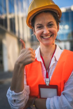 Mimar kadın inşaat mühendisi dışarıda duruyor ve modern bina duvarının önünde koruyucu başlık takıyor.