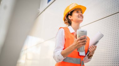 Mimar kadın inşaat mühendisi dışarıda duruyor ve modern bina duvarının önünde koruyucu başlık takıyor.