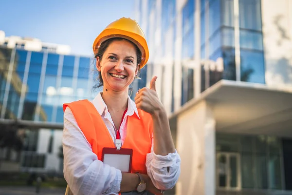 architect woman female construction engineer stand outdoors wear protective helmet and west in front of modern building wall