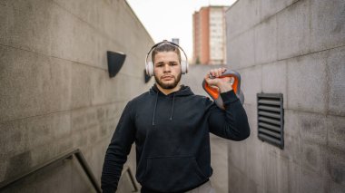 Kafkasyalı genç bir erkek sporcu gün içinde dışarıda Rus çanı Girya Kettlebell ağırlığında gerçek bir insan gibi poz veriyor.