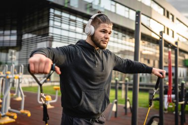 Yetişkin beyaz bir adam, günlük egzersiz rutininde lastik elastik direnç tüpleri kullanarak şehir dışında antrenman yapıyor. Gerçek insan sağlığı ve fitness konsepti kopyalama alanı kullanıyor.