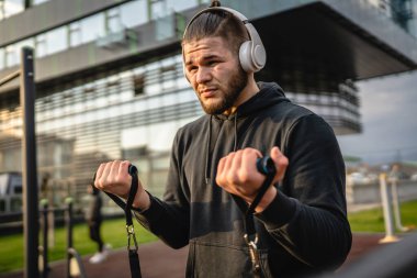 Yetişkin beyaz bir adam, günlük egzersiz rutininde lastik elastik direnç tüpleri kullanarak şehir dışında antrenman yapıyor. Gerçek insan sağlığı ve fitness konsepti kopyalama alanı kullanıyor.