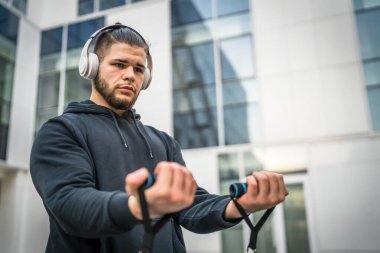 Yetişkin beyaz bir adam, günlük egzersiz rutininde lastik elastik direnç tüpleri kullanarak şehir dışında antrenman yapıyor. Gerçek insan sağlığı ve fitness konsepti kopyalama alanı kullanıyor.