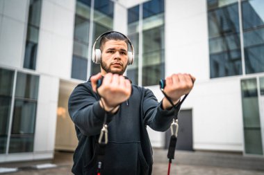 Yetişkin beyaz bir adam, günlük egzersiz rutininde lastik elastik direnç tüpleri kullanarak şehir dışında antrenman yapıyor. Gerçek insan sağlığı ve fitness konsepti kopyalama alanı kullanıyor.