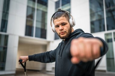 Yetişkin beyaz bir adam, günlük egzersiz rutininde lastik elastik direnç tüpleri kullanarak şehir dışında antrenman yapıyor. Gerçek insan sağlığı ve fitness konsepti kopyalama alanı kullanıyor.